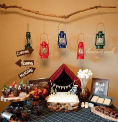 a table topped with cakes and desserts next to hanging signs that say camping is coming