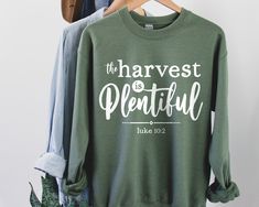 "Inspire others this fall with a super comfy sweatshirt featuring the words \"The Harvest is Plentiful\" from Luke 10:2! Also available as a T-shirt: https://www.etsy.com/listing/844626346/the-harvest-is-plentiful-shirt-luke-102 **This is an original design created by The Creative Cloth. Thanks for shopping with the original designer GARMENT INFO These are Gildan heavy blend sweatshirts! - The perfect mix of 8oz 50% cotton and 50% polyester - Made using pill-resistant air jet yarn - Double-needl Inspirational Letter Print Sweatshirt For Fall, Inspirational Text Print Fall Sweatshirt, Inspirational Crew Neck T-shirt For Fall, Inspirational Slogan Sweatshirt For Fall, Inspirational Text Print Sweatshirt For Fall, Fall Green Sweatshirt With Slogan, Green Slogan Sweatshirt For Fall, Fall Inspirational Graphic Print Sweatshirt, Inspirational Graphic Print Fall Sweatshirt