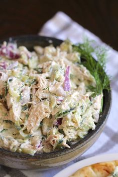 a bowl filled with chicken salad next to two slices of pizza on a tablecloth