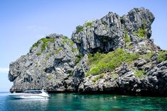 a boat is in the water next to some rocks and green vegetation on an island