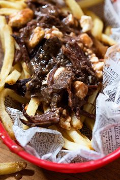 a red basket filled with french fries covered in meat and sauce on top of paper