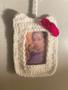 a crocheted photo frame hanging on a wall with a red flower in it