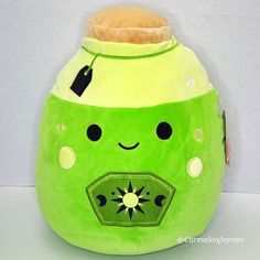 a green stuffed animal with a tag on it's chest and eyes, sitting against a white background