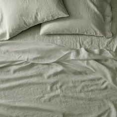 an unmade bed with white sheets and pillows