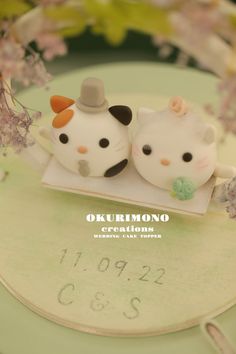 two small white cats sitting on top of a table next to each other with flowers in the background