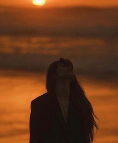 a woman standing on the beach at sunset looking up into the sky with her eyes closed