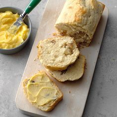 two loaves of bread with butter on a cutting board next to a small bowl