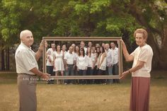 an older man and woman holding up a large framed photo in front of them with people behind them