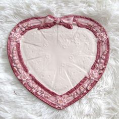 a heart shaped dish with pink trim and bows on it sitting on a white furnishing