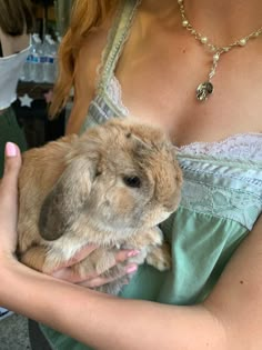 a woman holding a small rabbit in her arms while wearing a green dress and necklace