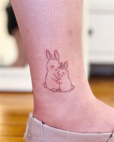 a small tattoo on the ankle of a woman's foot with a rabbit hugging her head