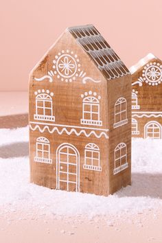 two wooden houses sitting in the snow on top of a pink surface with one house cut out