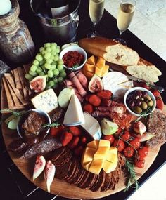 an assortment of cheeses and meats on a wooden platter with wine glasses