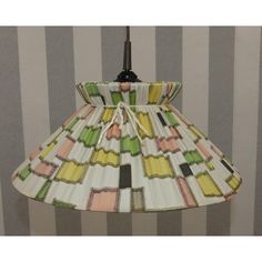 a lampshade hanging from a wall with striped walls behind it and a lamp shade in the middle