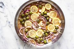 a pan filled with sliced lemons, olives and onions on top of a marble counter