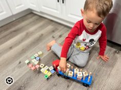 a toddler playing with wooden blocks on the floor in front of an oven and dishwasher