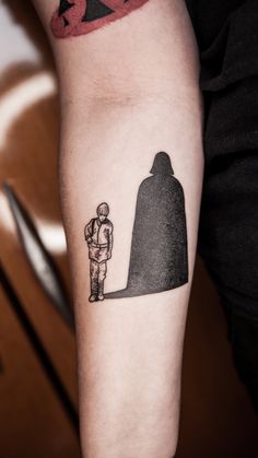 a person with a small tattoo on their arm next to a giant black piece of art