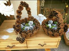 two baskets filled with pine cones and flowers on top of a wooden table next to a basket