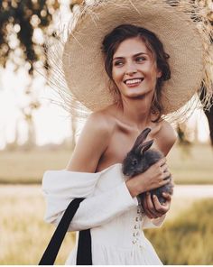 a woman wearing a straw hat holding a rabbit in her arms and smiling at the camera