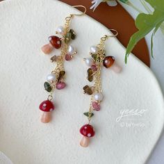 a pair of dangling earrings with pearls and beads on a white plate next to flowers