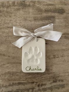 a white ceramic ornament with a ribbon on it and a paw print in the center