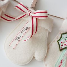 two mittens hanging from a clothes line with a name tag on them and a pair of scissors next to it