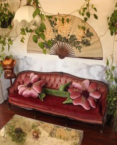 a red couch with pink flowers on it in front of a fan and other decorations