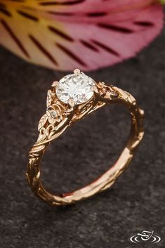 a gold ring with a diamond in the center on a table next to a flower