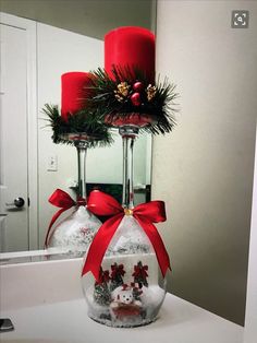 two red candles sitting on top of a white counter next to a bottle with christmas decorations