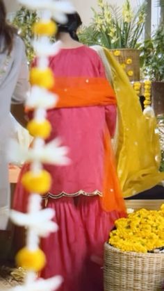 a woman in a pink dress standing next to a basket filled with yellow and white flowers