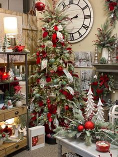 a christmas tree with red and green ornaments in front of a large clock on the wall