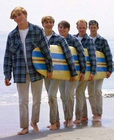 four young men are holding surfboards on the beach