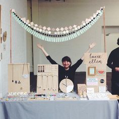 a woman standing behind a table with lots of crafting supplies on it