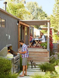 a man standing in front of a bbq next to a woman and two cats