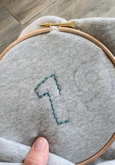 someone is stitching the letter f on top of a gray pillow with blue thread