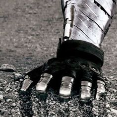 a black and white photo of a person's foot in dirt with metal gloves on