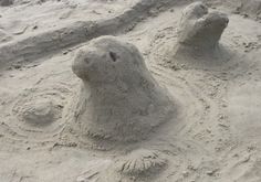 sand sculptures made to look like bears on the beach, with one bear's head sticking out of the sand