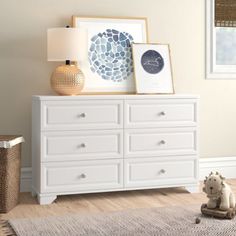 a white dresser sitting in a bedroom next to a lamp and pictures on the wall