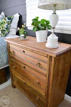 a dresser with two potted plants on top of it and a lamp next to it