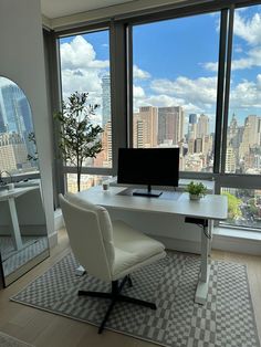 a desk with a computer on top of it in front of large windows overlooking the city