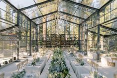 the inside of a greenhouse with tables and chairs covered in white cloths, surrounded by greenery