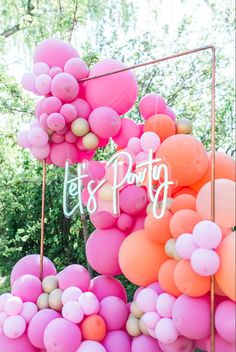 pink and orange balloons with let's party written on them are hanging from a metal frame