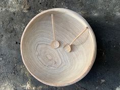 a wooden clock sitting on top of a cement floor next to two sticks sticking out of it