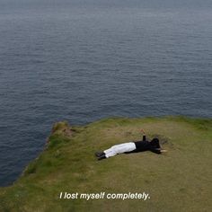 a man laying on top of a lush green hillside next to the ocean with a quote written below