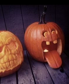 two carved pumpkins sitting on top of a wooden table next to each other, one with its mouth open