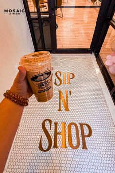 a hand holding a cup of coffee in front of a sign that says sip n'shop