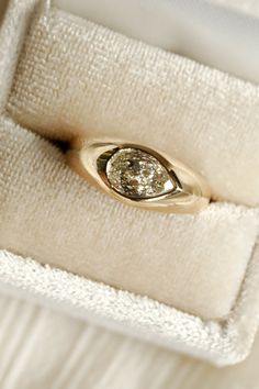 a gold ring with a diamond in it sitting on a white cloth box that is open