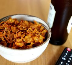 a white bowl filled with fried food next to a bottle of beer and remote control