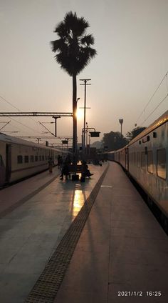 two trains are parked at the train station as the sun is setting in the background