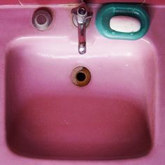 a pink sink in a bathroom with green handles